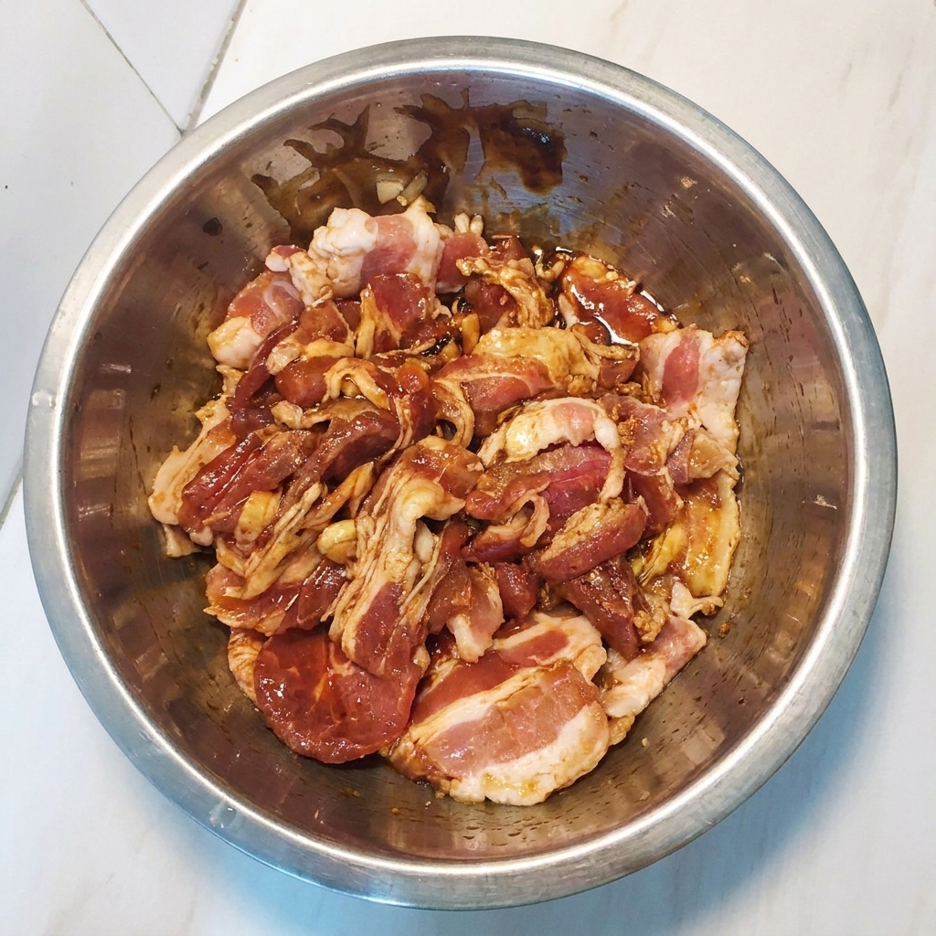 Tranches de poitrine de porc marinées mélangées dans un bol en métal pour assurer un enrobage uniforme.