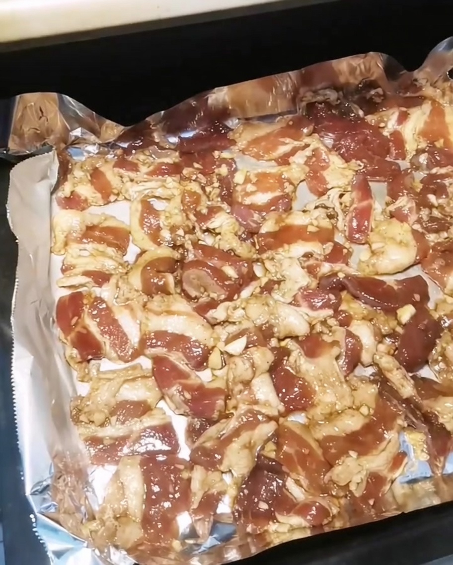 Une plaque de cuisson remplie de tranches de poitrine de porc assaisonnées insérée dans un four chaud.