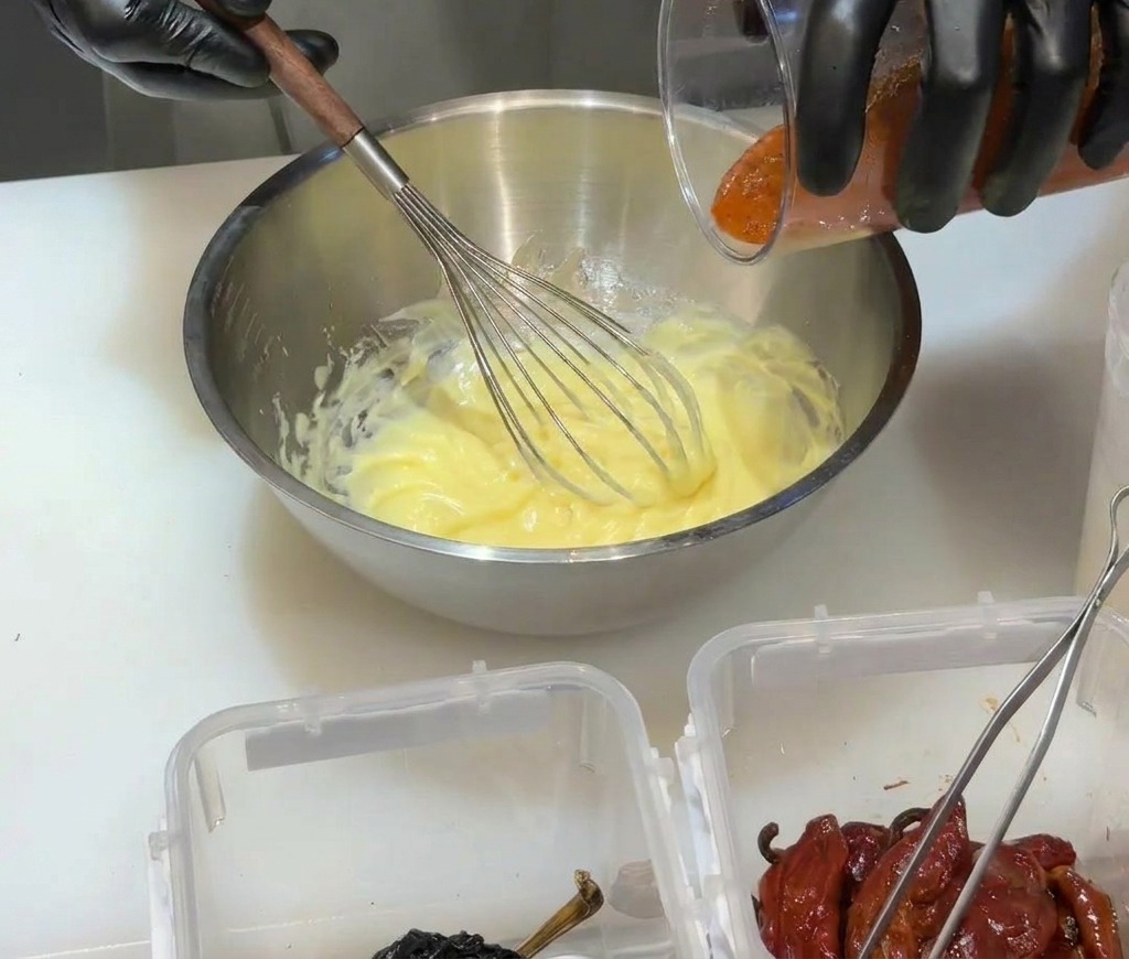 Verser la purée de piment rouge mixée dans une base de mayonnaise jaune dans un bol en métal.