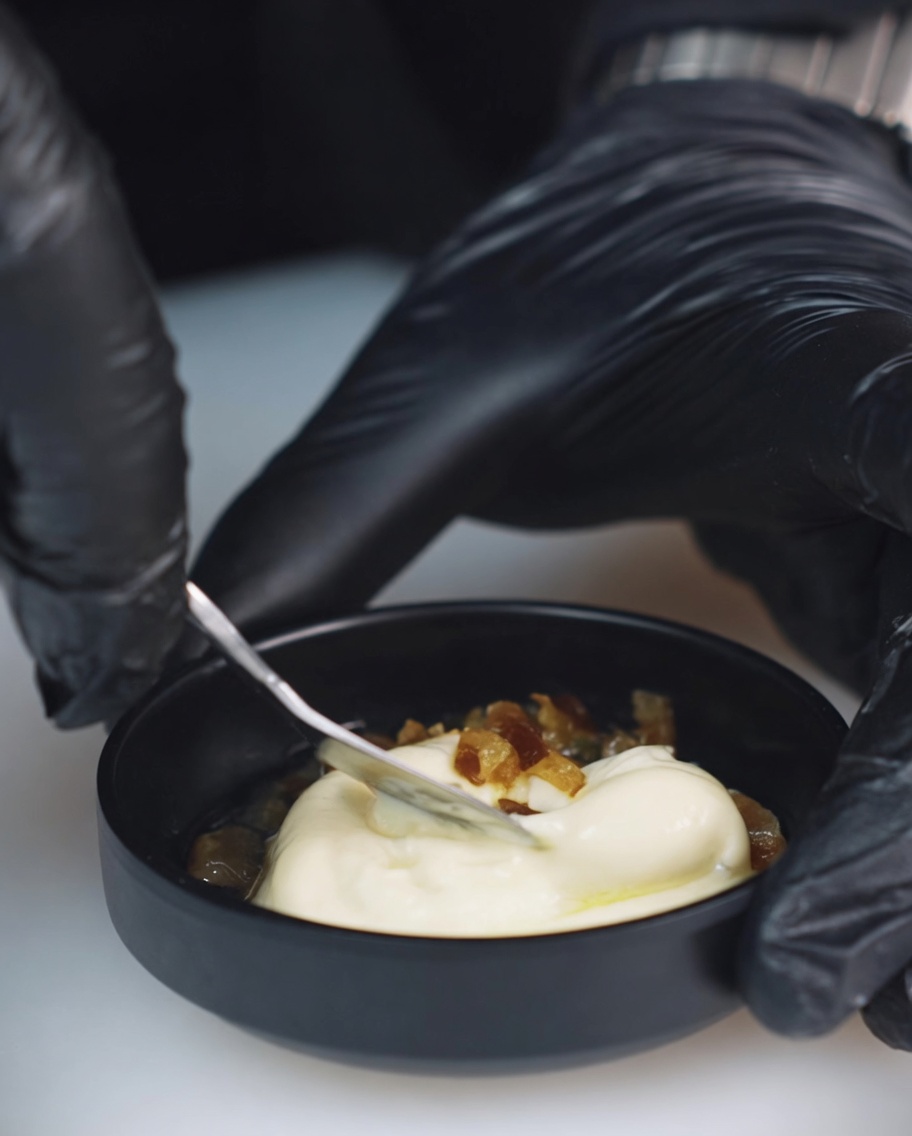 Gros plan sur un petit bol contenant de la mayonnaise, des piments mexicains hachés et du jus de cornichons mélangés avec une cuillère en métal.