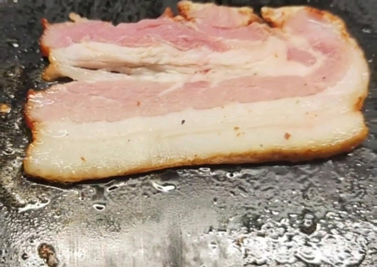 Une tranche de bacon grésillant et cuisant sur une plaque chaude.