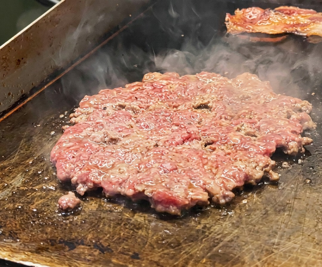 Un steak de bœuf fin saisissant sur la plaque, assaisonné de sel et garni de tranches doignon.