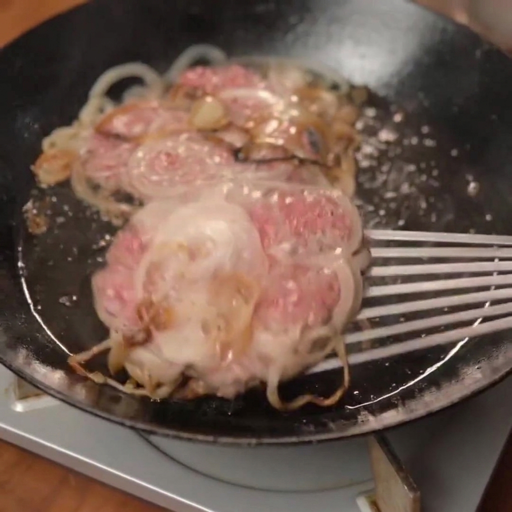 Un palet de smash burger chaud et recouvert de fromage fondu en train dêtre placé sur un pain toasté.