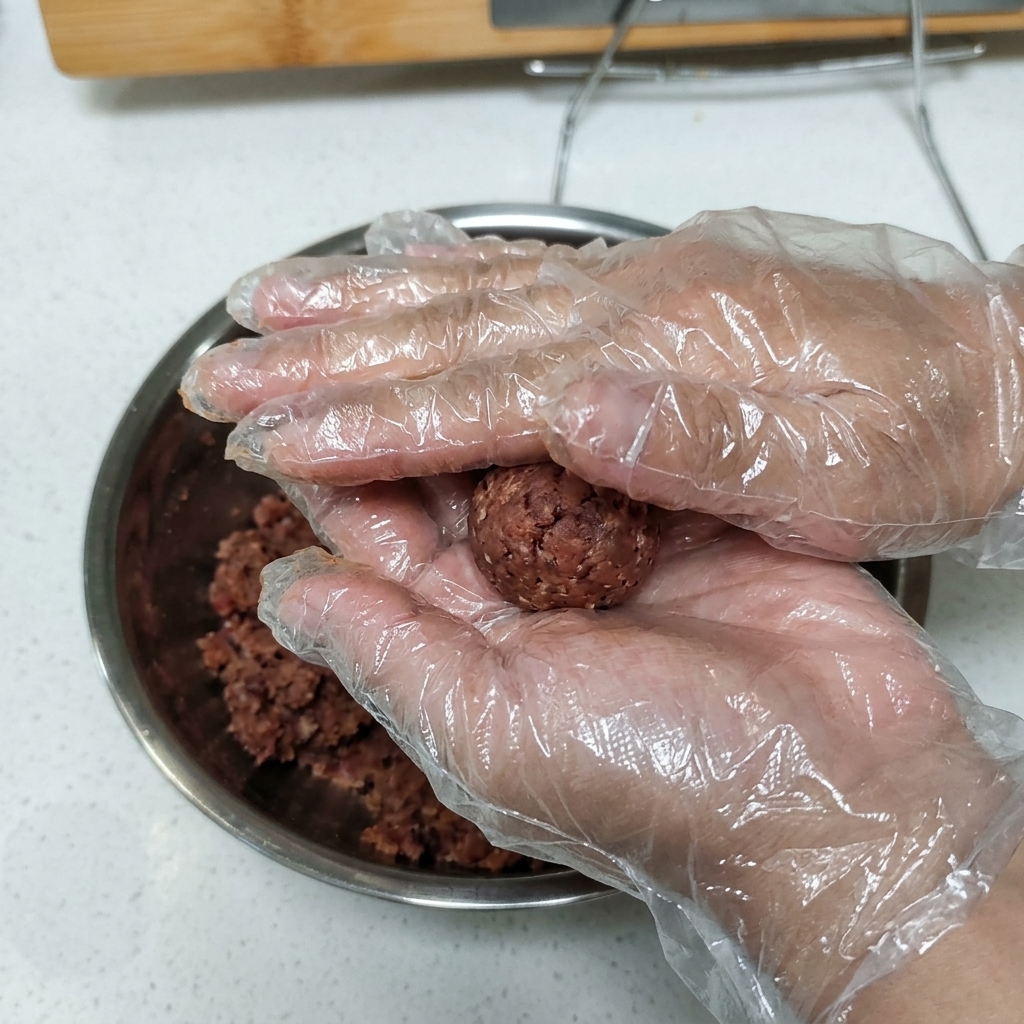 Des mains gantées tenant et pressant une boule de bœuf haché assaisonné pour lui donner une forme de steak.