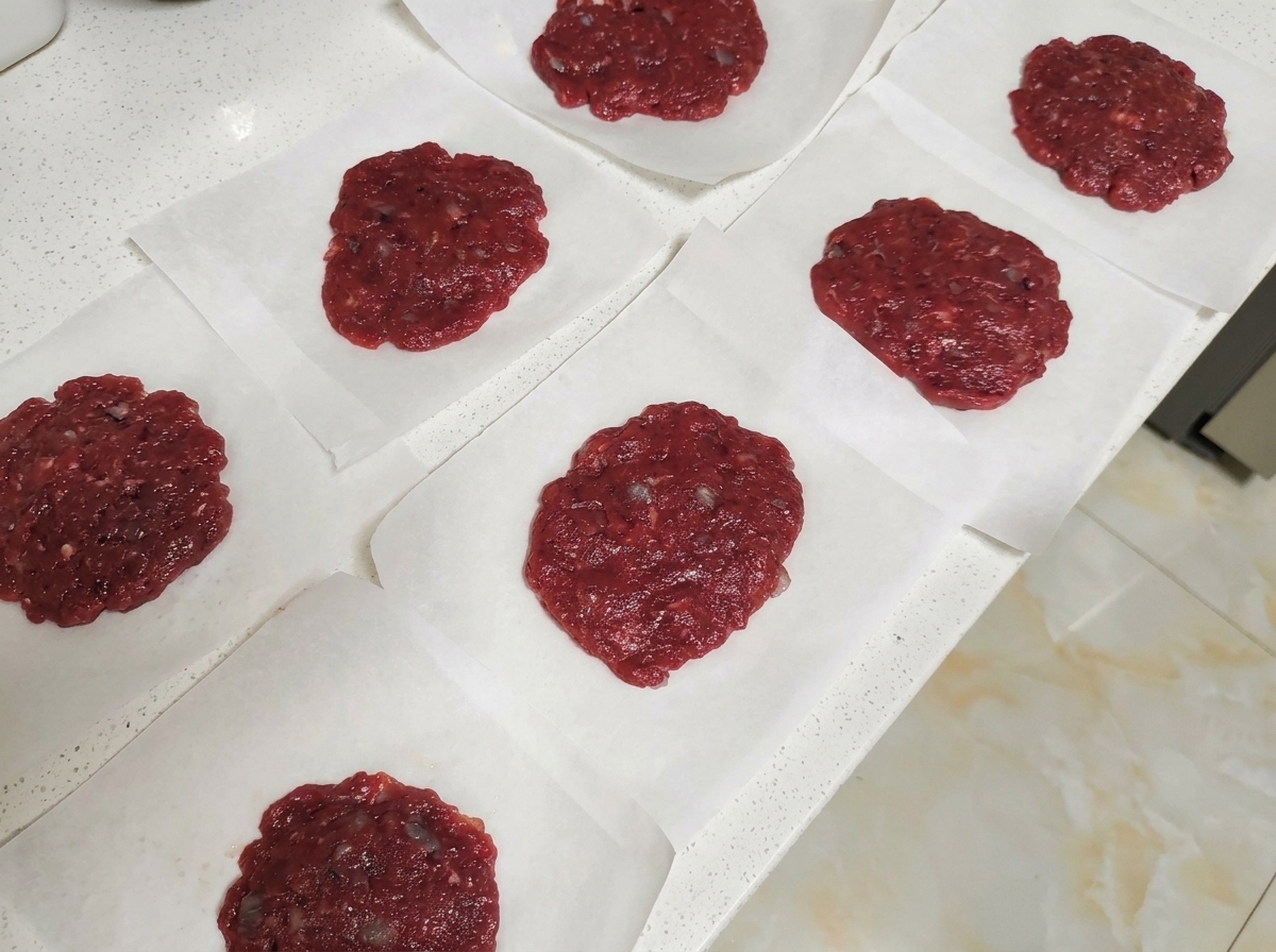 Plusieurs steaks de bœuf crus disposés individuellement sur des carrés de papier sulfurisé sur un plan de travail clair.