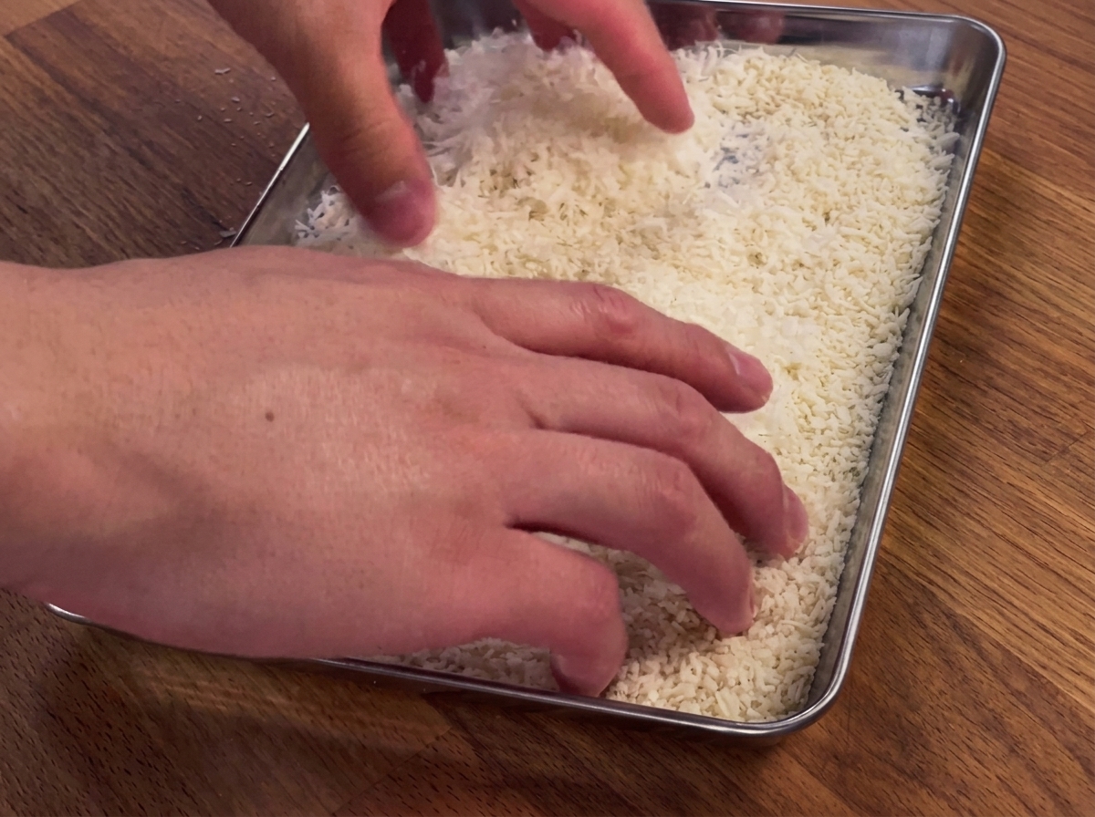 Des mains pressant un blanc de poulet dans un plateau de chapelure et de parmesan.