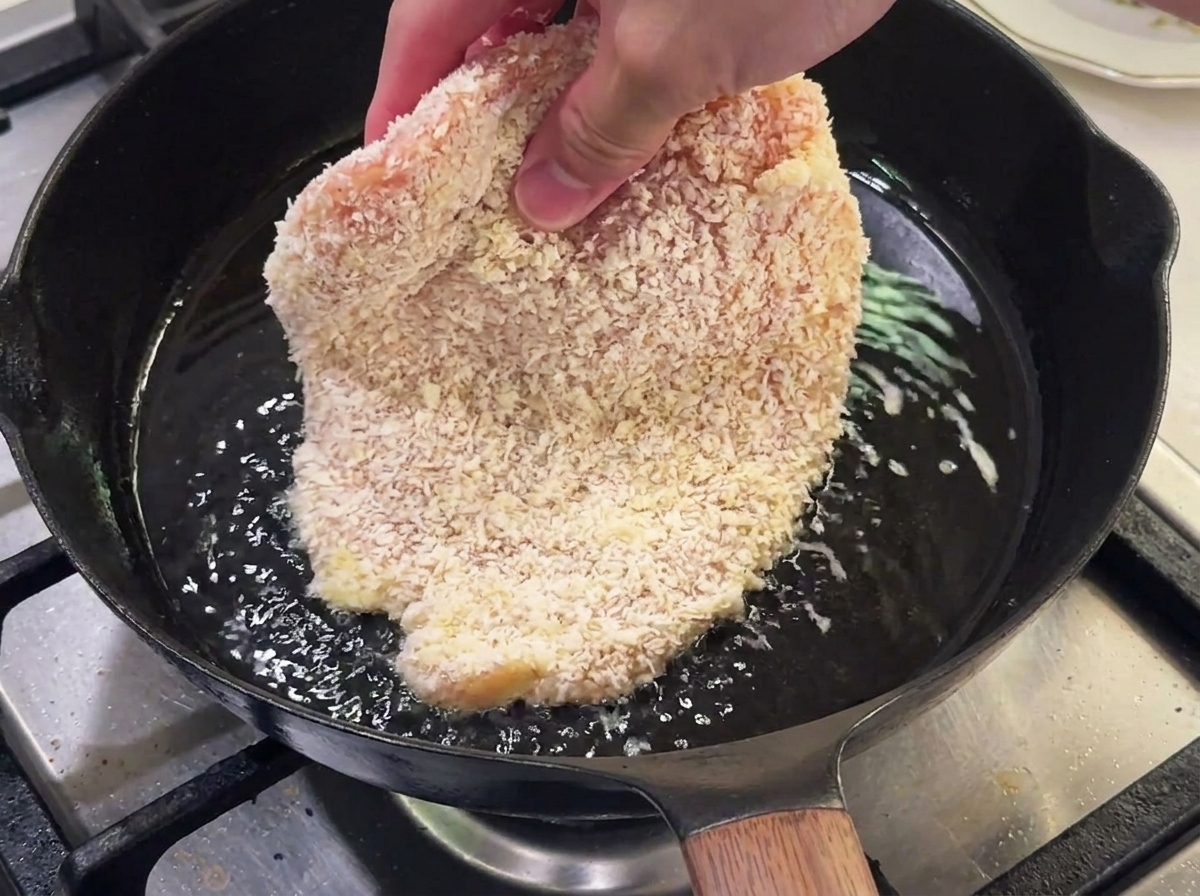 Blanc de poulet pané en train de frire dans une poêle avec de lhuile chaude.