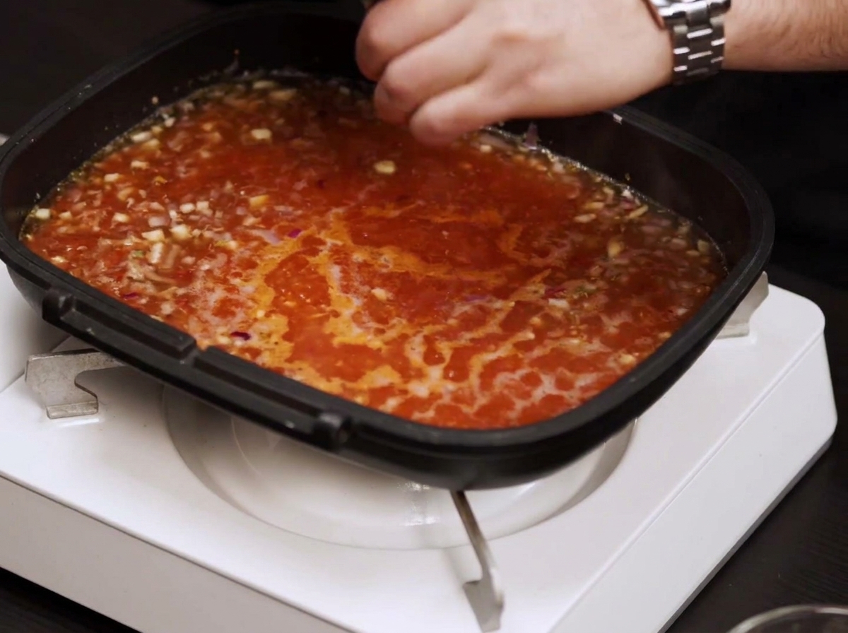 Poêle remplie dune sauce tomate rouge frémissante assaisonnée avec du sel et du poivre.