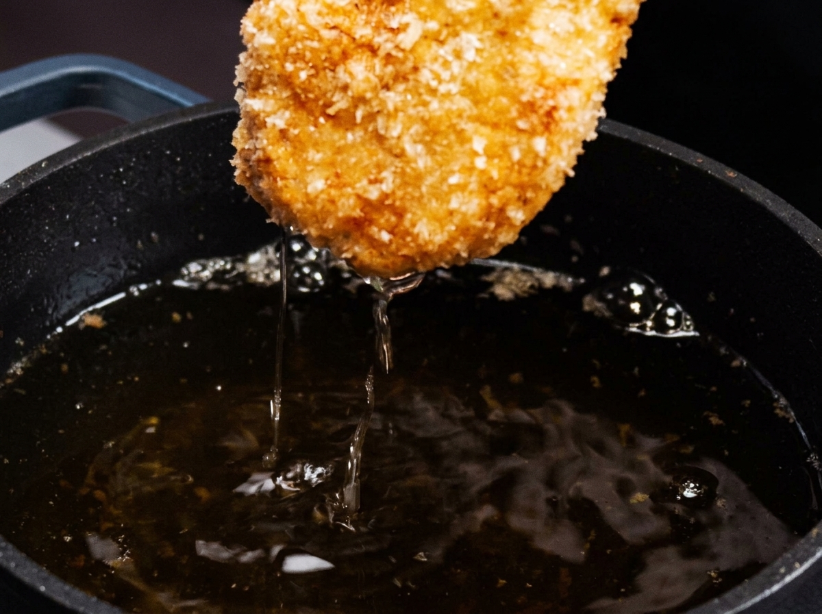 Escalope de poulet panée retirée dune poêle avec une croûte dorée.