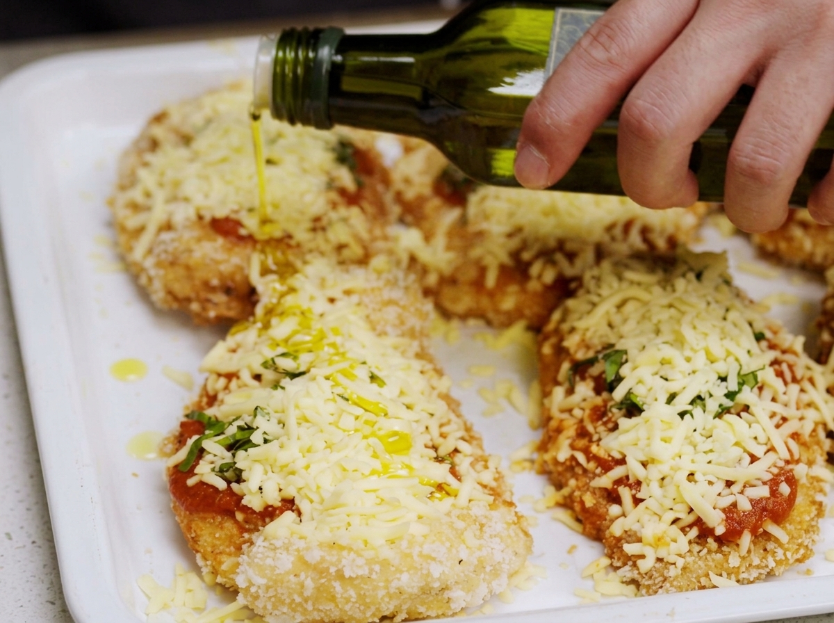 Huile dolive versée sur le plat de poulet au parmesan prêt à être enfourné.