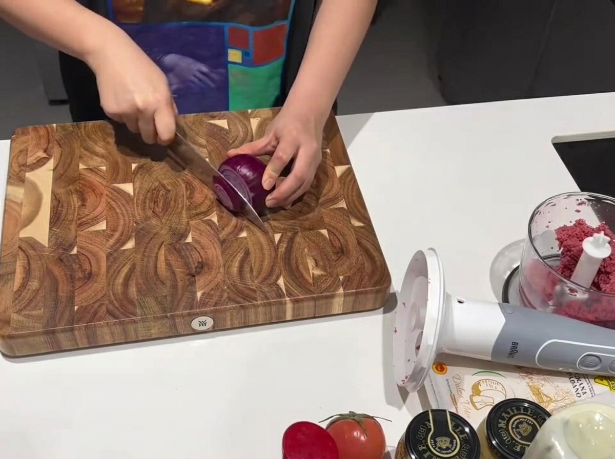 Un couteau de cuisine tranchant coupant un oignon rouge frais sur une planche à découper en bois.