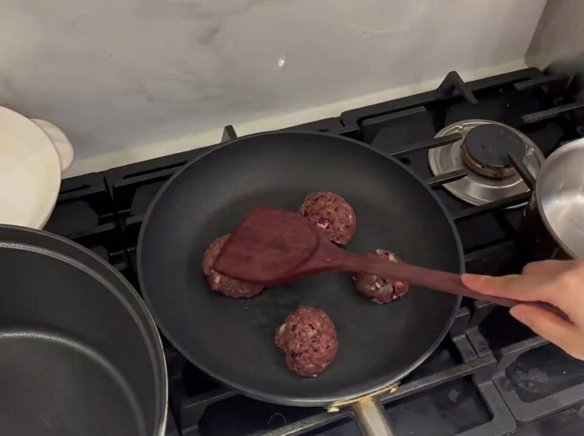Boulettes de bœuf écrasées dans une poêle chaude à laide dune spatule en métal.