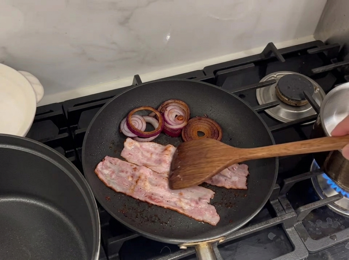 Tranches de bacon et anneaux doignon rouge en train de frire dans une poêle.