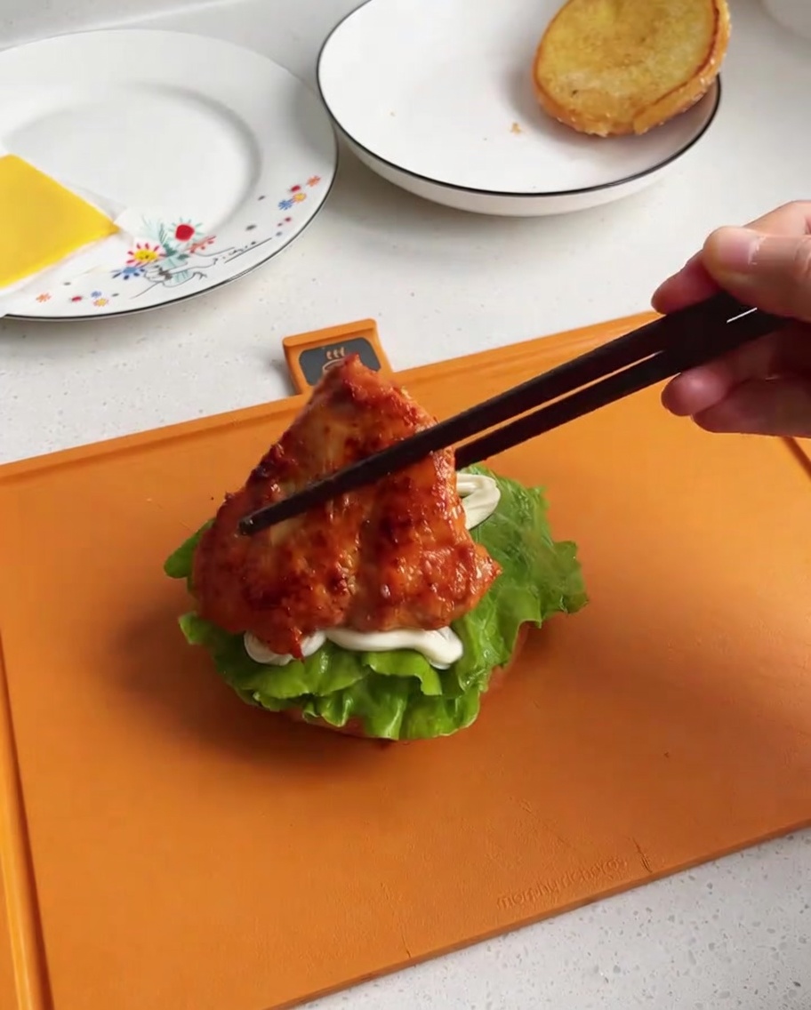 Un morceau de poulet cuit et glacé placé sur la base du burger avec de la laitue et de la mayonnaise.
