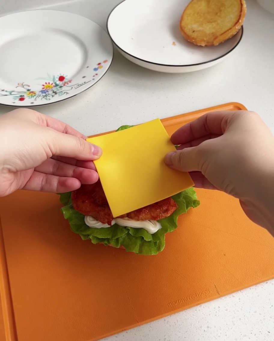 Une tranche de fromage jaune centrée sur le morceau de poulet chaud sur la base du burger.