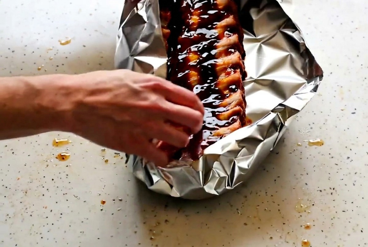 Mains pliant et scellant les bords de la papillote en aluminium.