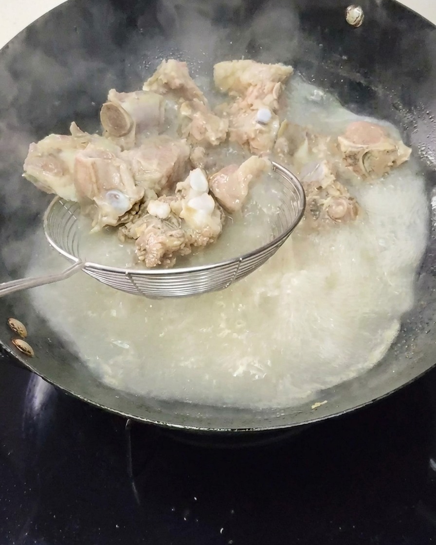 Travers de porc blanchis retirés de leau bouillante avec une écumoire.