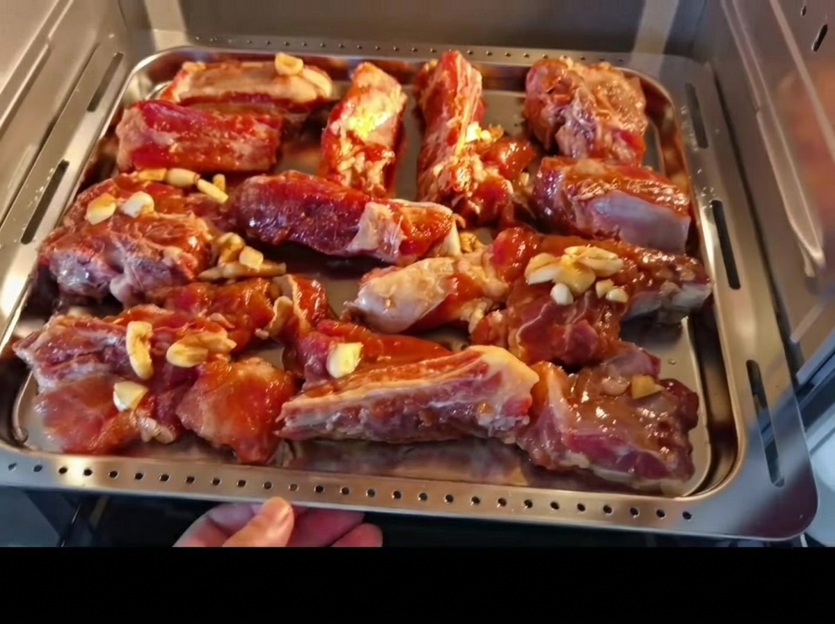 Travers de porc marinés disposés sur une plaque de cuisson en métal, sur le point dêtre enfournés.