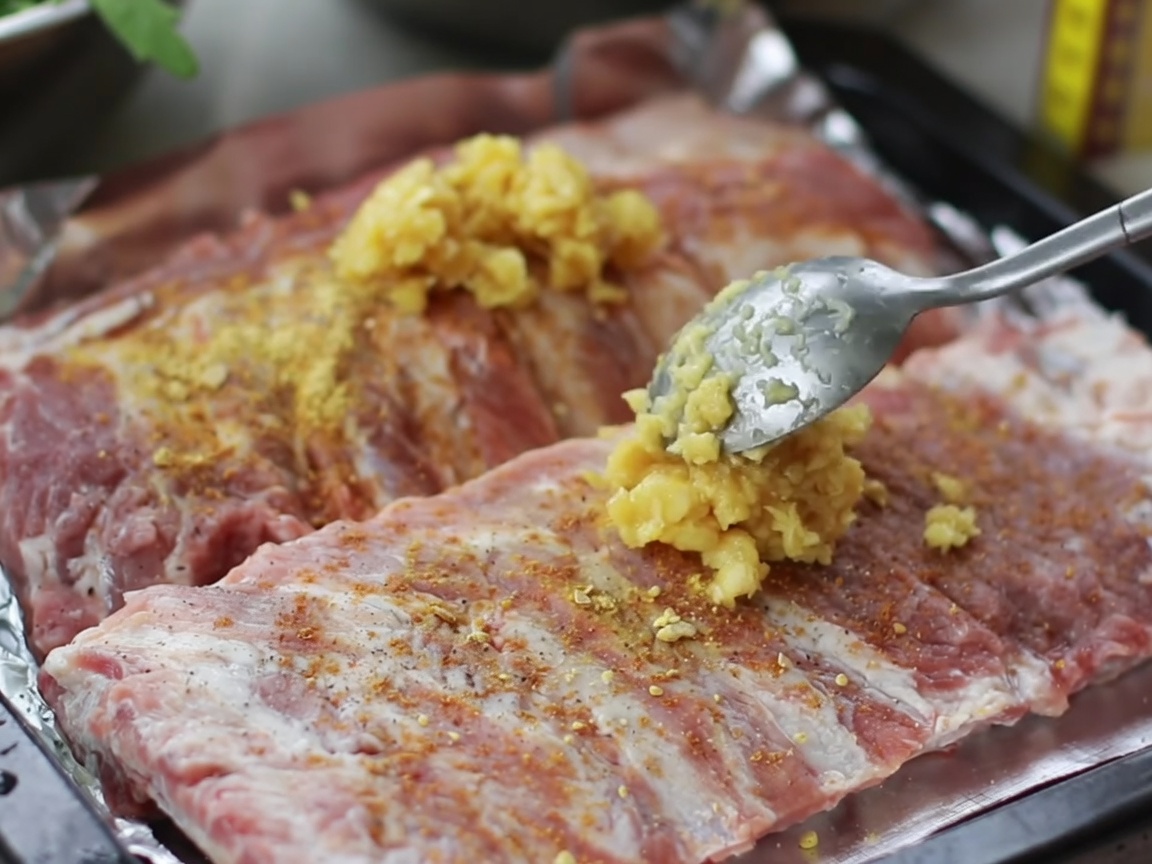 Mains massant un mélange dail haché et dépices sur la surface de travers de porc crus dans un plat.