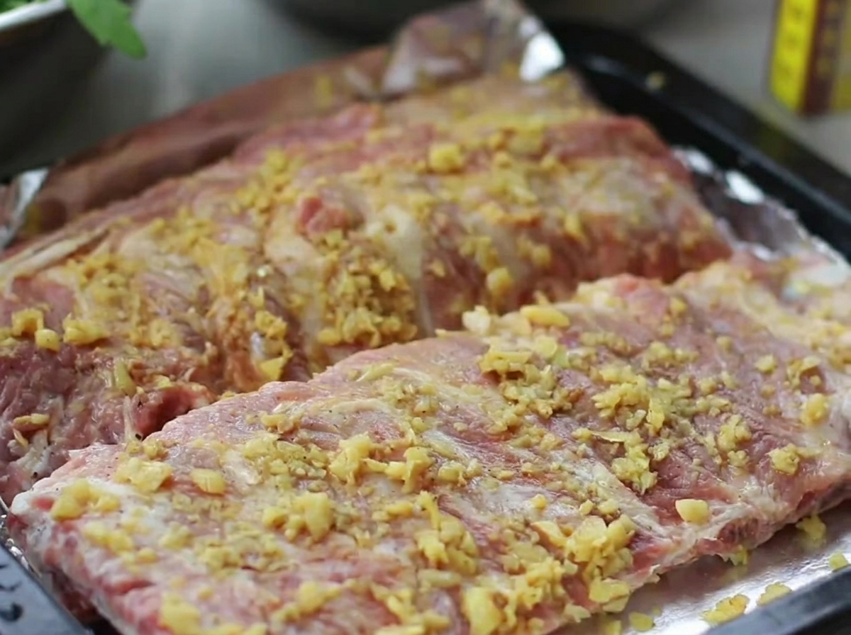 Un plat de cuisson contenant des travers de porc assaisonnés, hermétiquement fermé avec une couche de papier aluminium brillant.