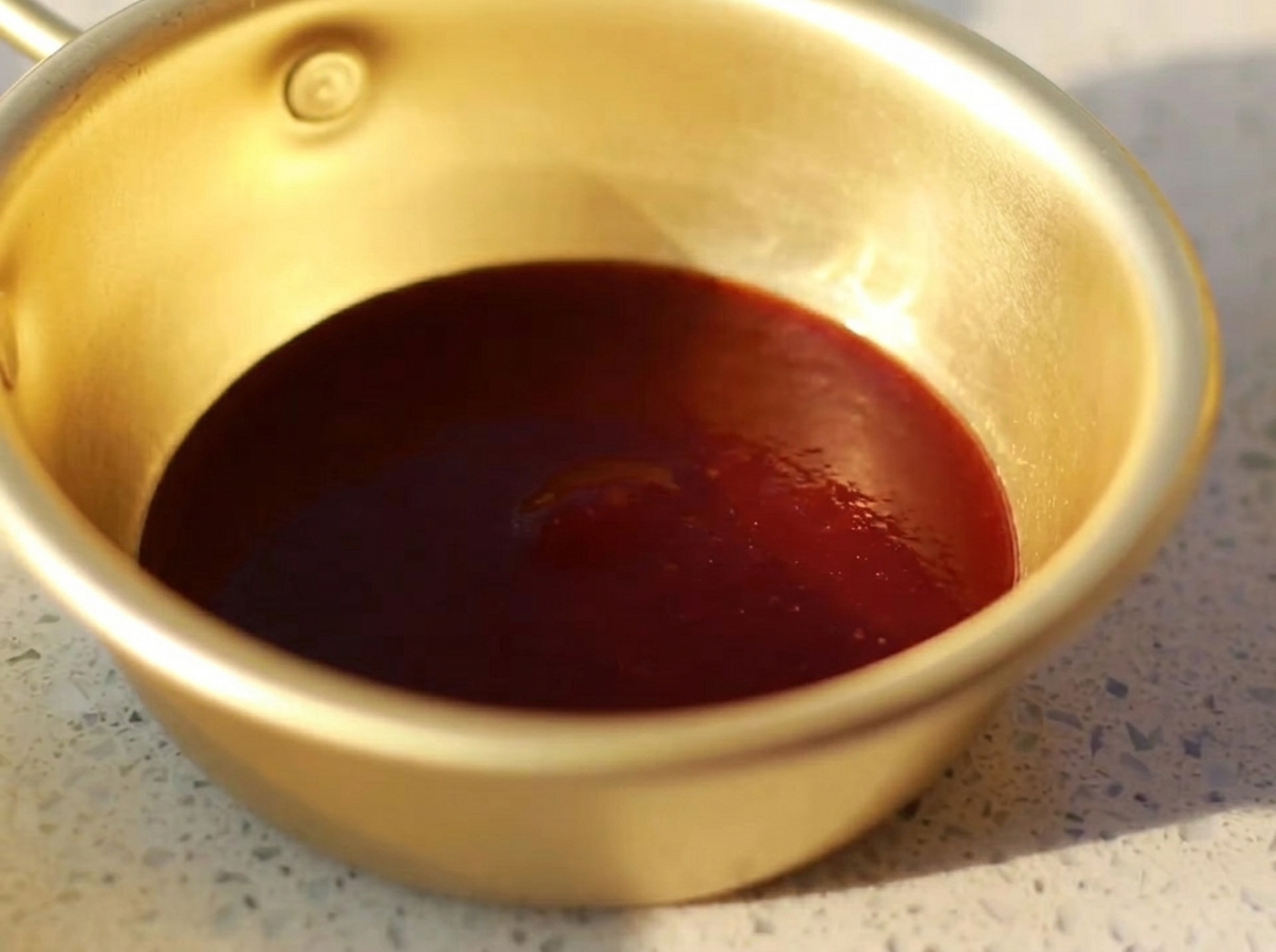 Un petit bol en métal contenant un mélange homogène de sauce barbecue, sauce huître, moutarde, miel et sauce soja claire.