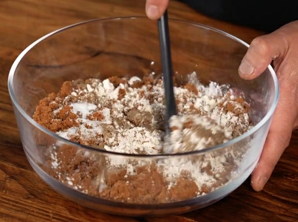 Un bol transparent contenant un mélange de cassonade, de poudre dail, de poivre noir et de sel, remué avec une spatule noire.