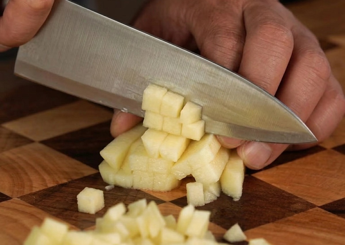 Une pomme fraîche soigneusement coupée en petits dés uniformes sur une planche à découper en bois.