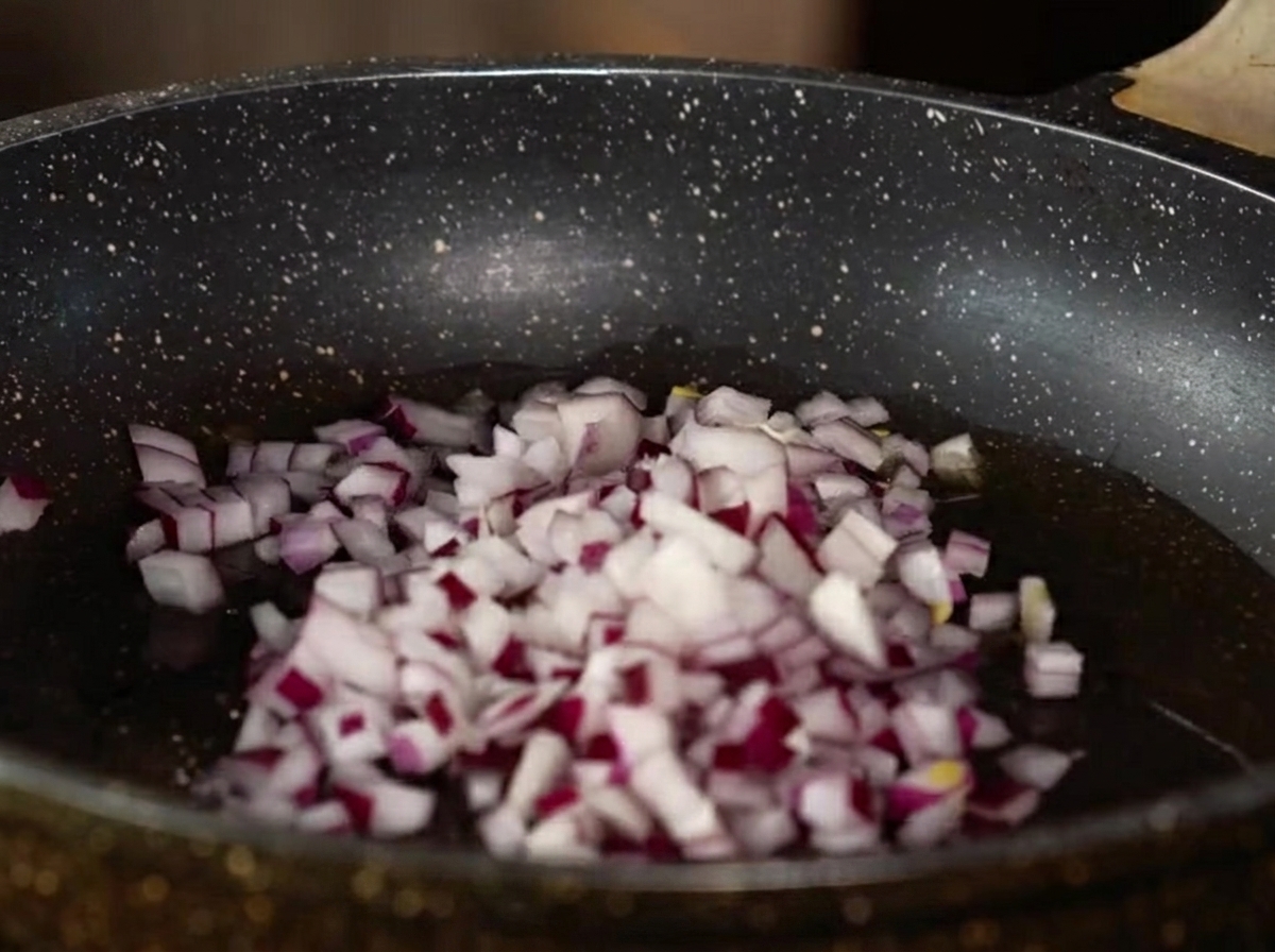Oignon rouge en dés, ail et gingembre hachés cuisant dans une poêle avec de lhuile.