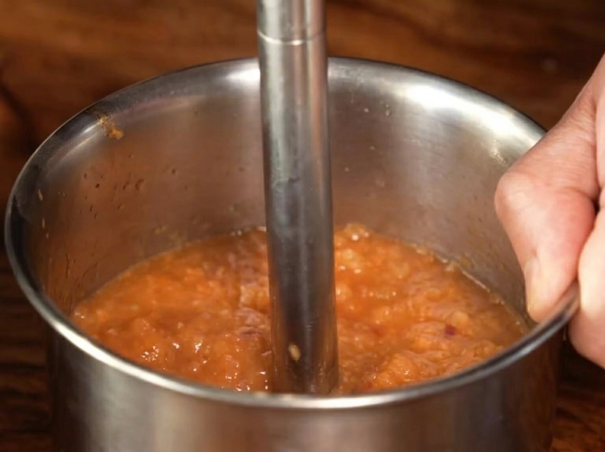 Un mixeur plongeant en métal transformant le mélange de sauce cuite en une purée lisse.