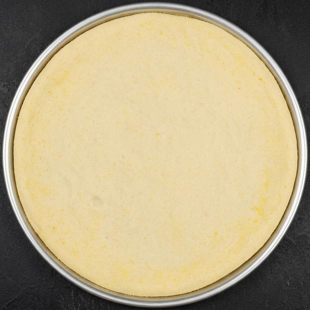 Un morceau rond de pâte à pizza dans un moule en métal, avec plusieurs incisions radiales sur le bord extérieur.