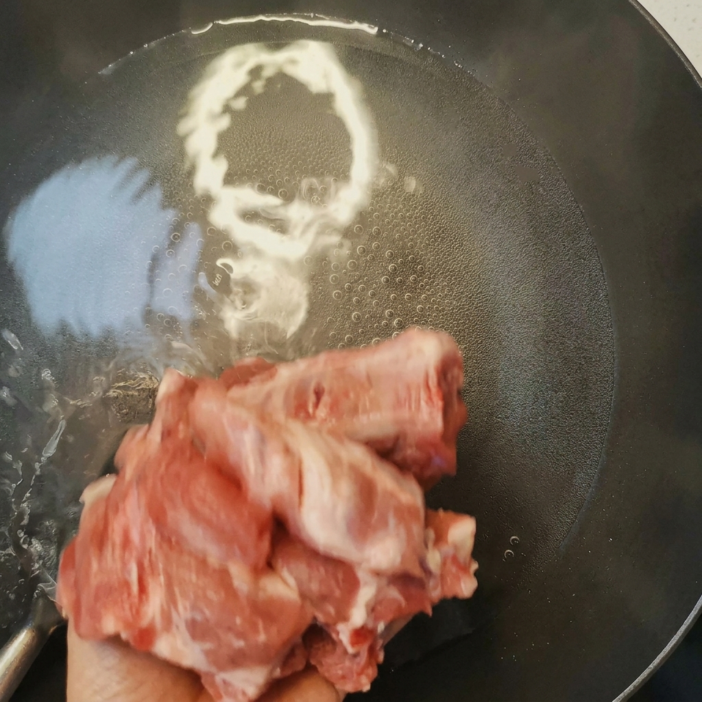 Travers de porc en train dêtre blanchis dans une casserole deau bouillante avec du vin de cuisine, montrant la mousse remontant à la surface.