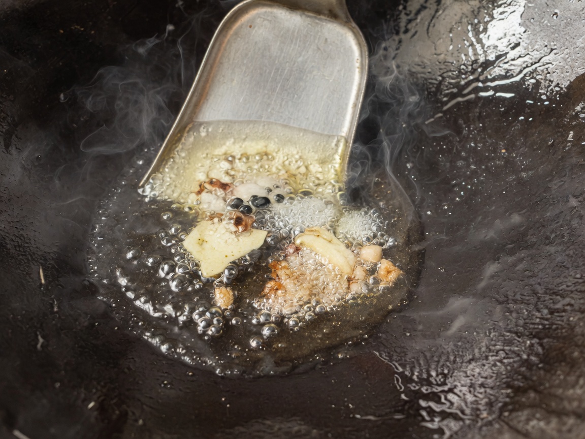 Aromates et épices grésillant dans lhuile chaude dans un wok culotté.