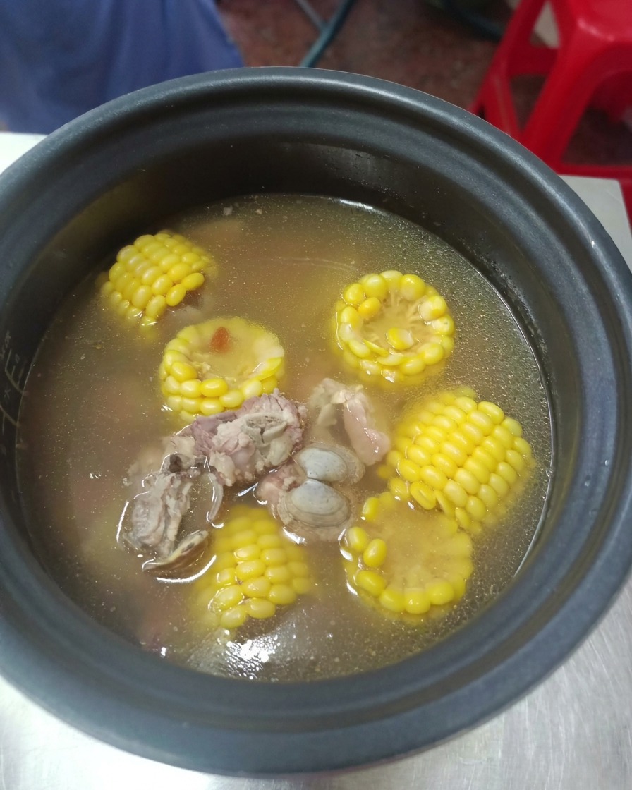 Un autocuiseur ouvert en toute sécurité révélant un bouillon clair fumant avec des travers de porc tendres et du maïs jaune vif.