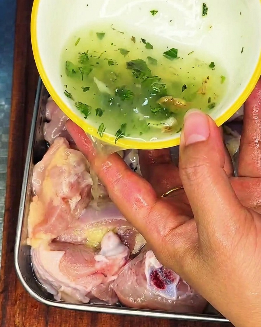 Une main versant un liquide aux oignons et gingembre sur du poulet cru dans un récipient.