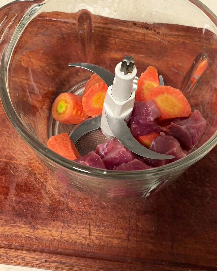 Morceaux de porc et dés de carottes dans le bol dun hachoir prêts à être mixés.