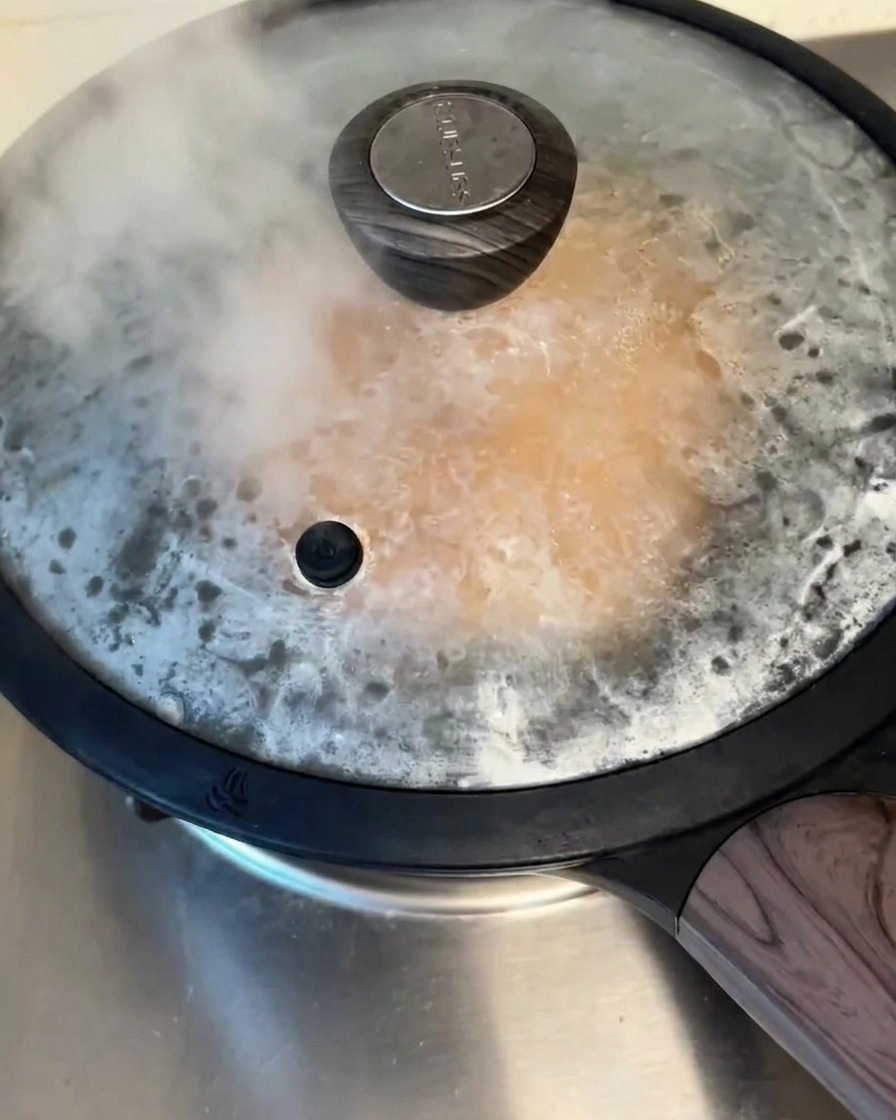 Une poêle antiadhésive couverte sur la cuisinière, avec de la vapeur séchappant sous le couvercle pendant que la crêpe cuit.