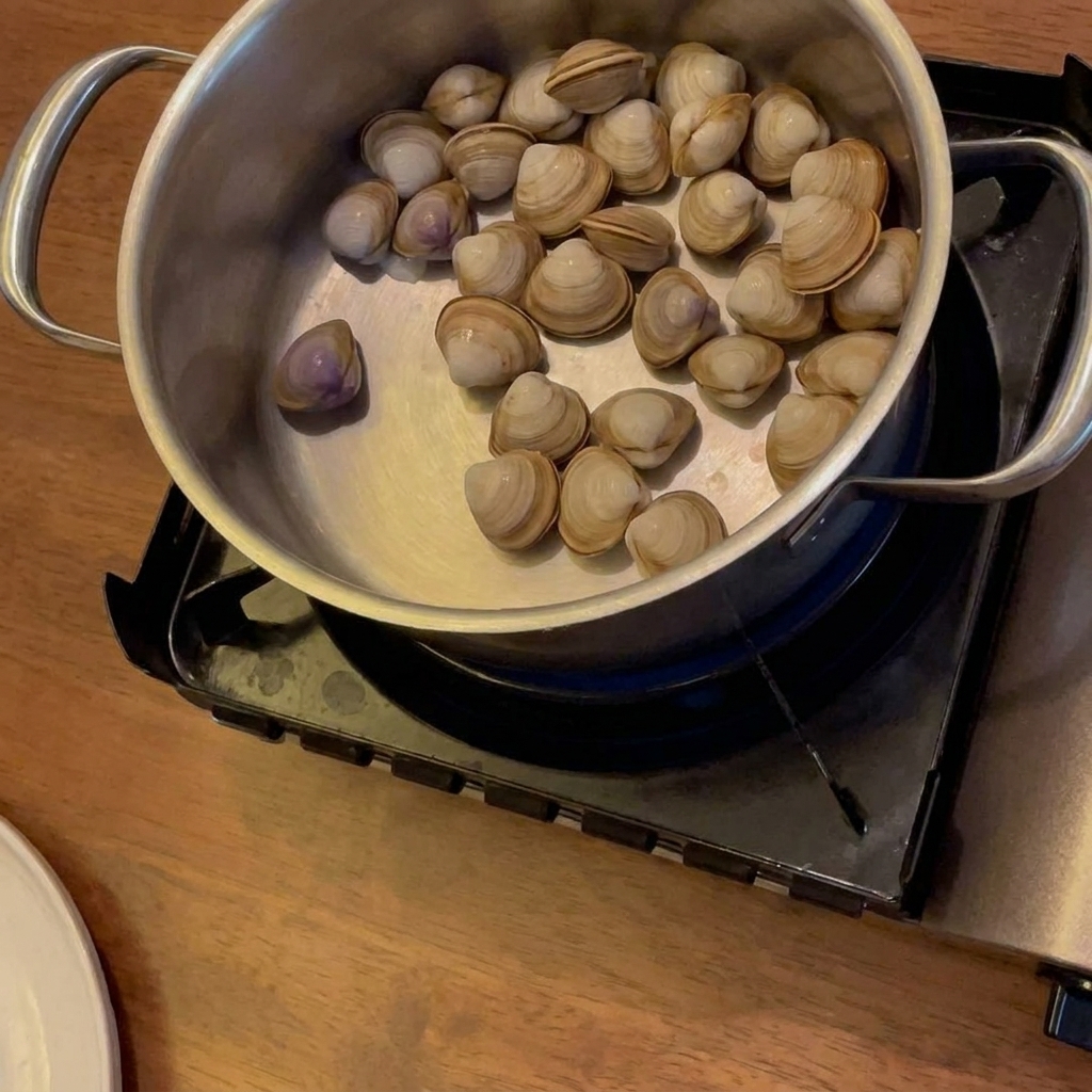 De lalcool versé dans une casserole avec des palourdes, des pommes de terre et des carottes sur un réchaud à gaz.