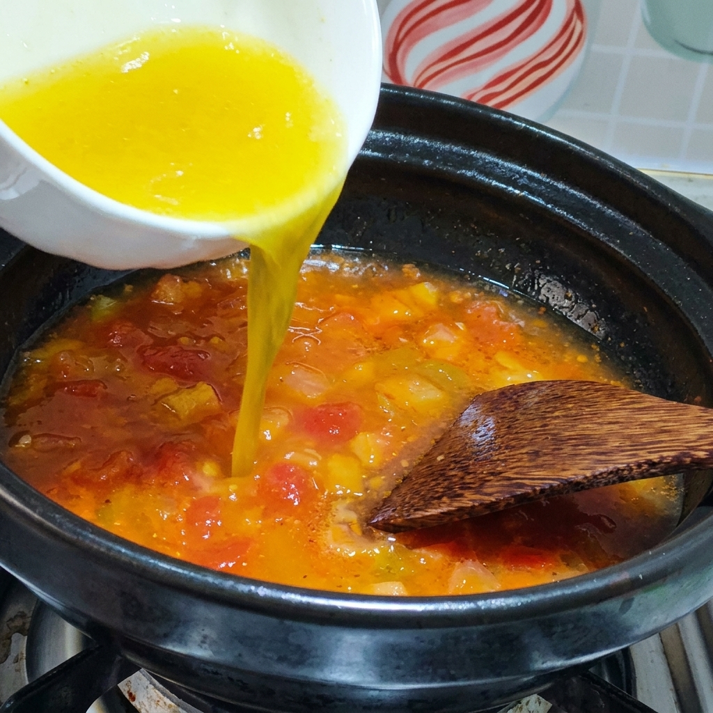 Le bouillon de poulet versé dans une marmite avec les tomates sautées.