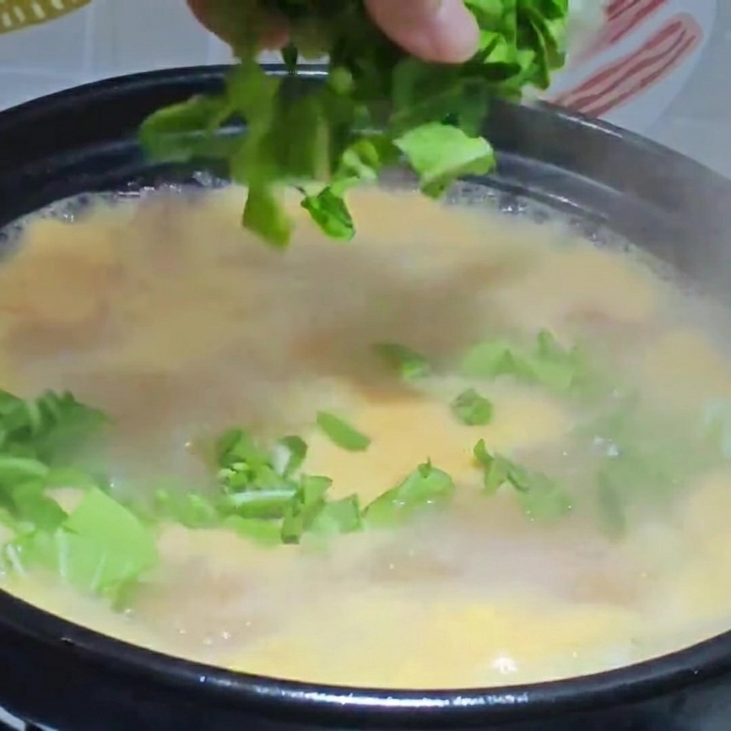 Légumes verts hachés et poulet effiloché ajoutés dans la marmite de soupe bouillante.
