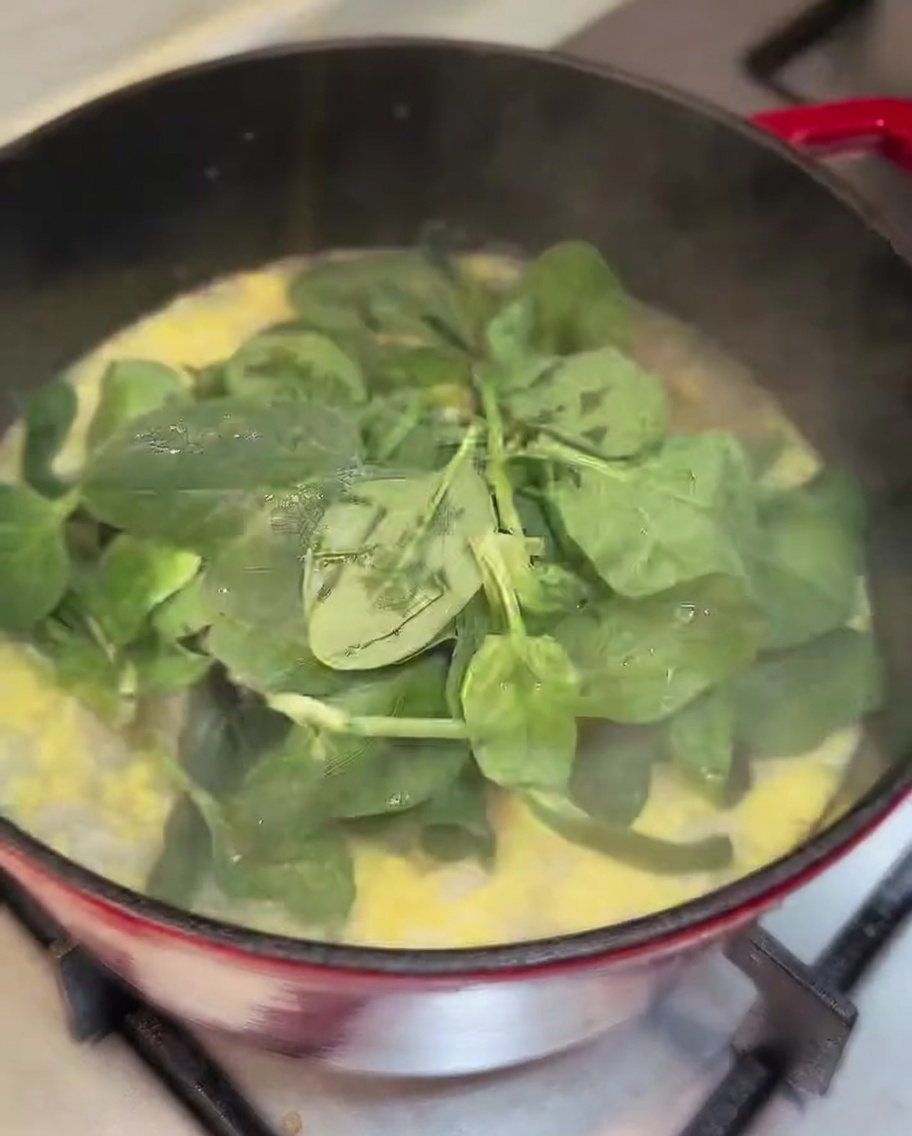 Feuilles dépinards frais incorporées dans une casserole de soupe au poulet finie.