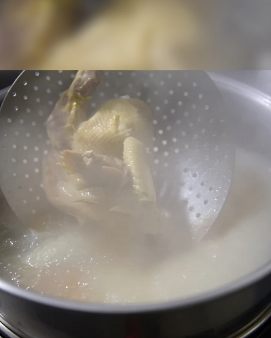 Un poulet cuit entier déposé délicatement dans un bouillon frémissant.
