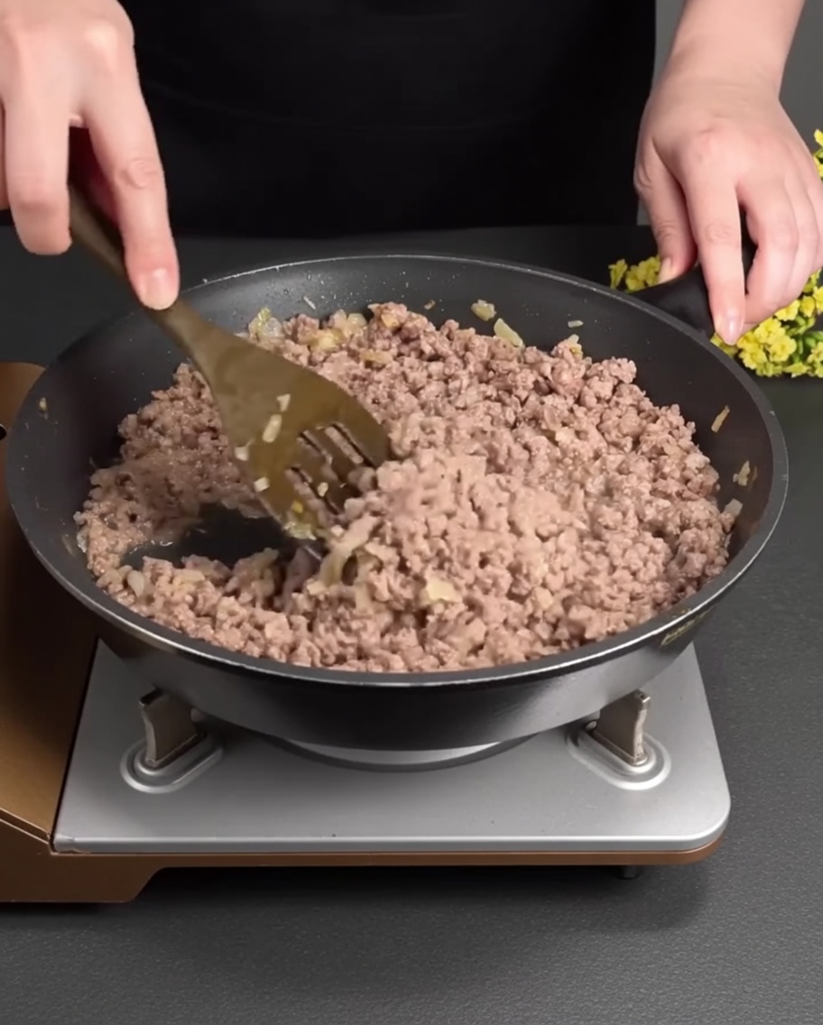Bœuf haché en train de brunir et dêtre émietté dans une poêle avec les aromates.
