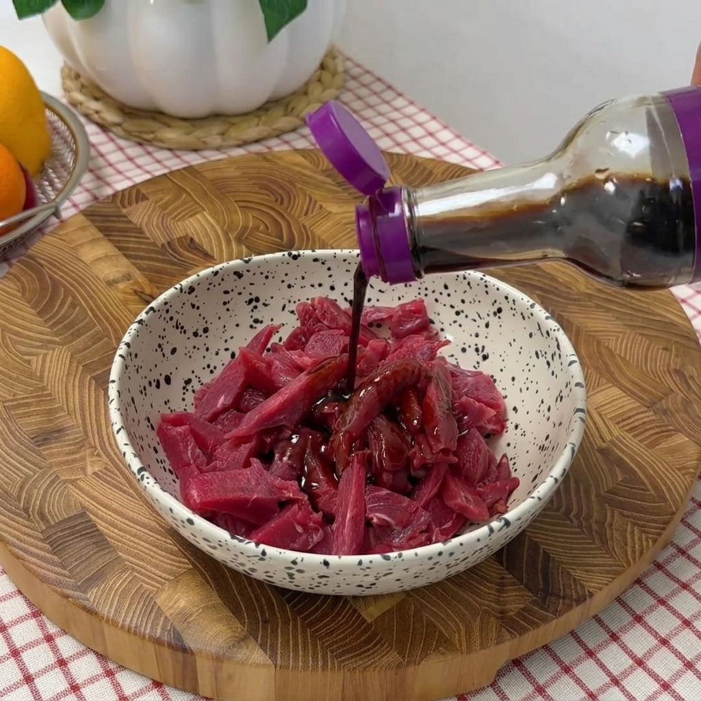 Lamelles de bœuf dans un bol assaisonnées avec sauce soja, poivre noir et huile.
