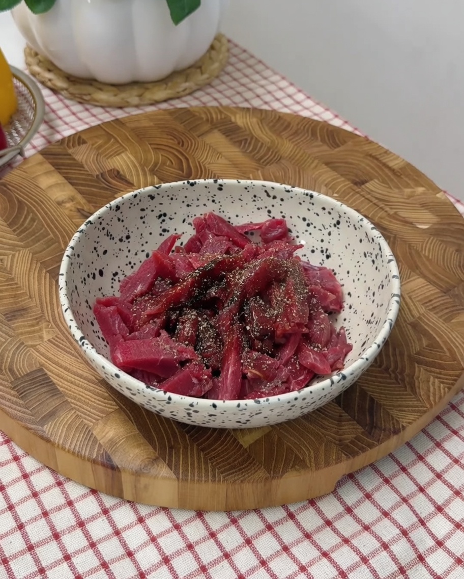 Main mélangeant les lamelles de bœuf assaisonnées dans un bol.