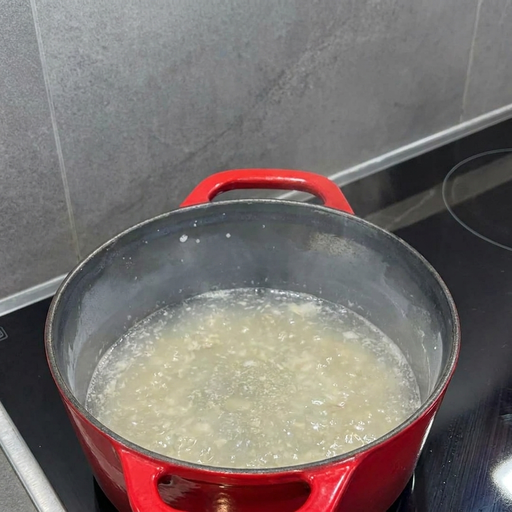 Lait versé dans le roux dans une casserole, avec un fouet mélangeant le tout en un liquide lisse.