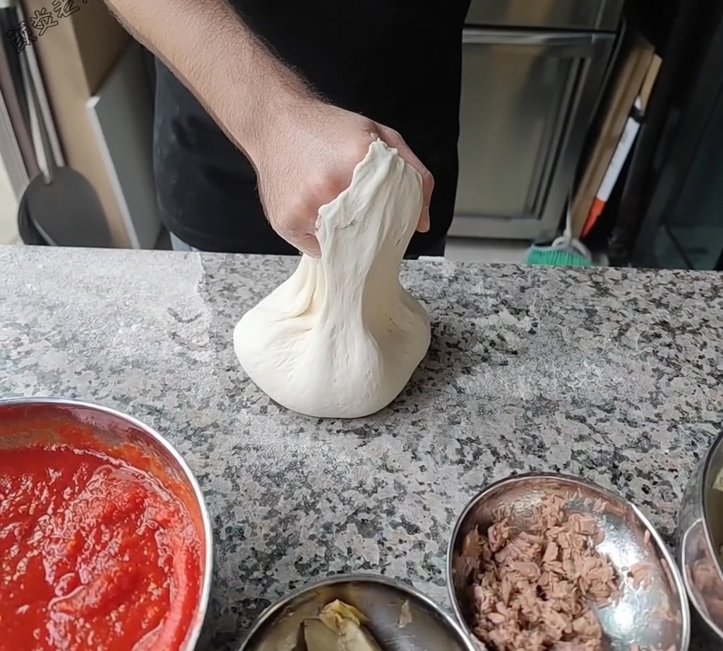 Le chef étire la pâte à pizza en la faisant tourner sur ses articulations pour atteindre le diamètre souhaité.