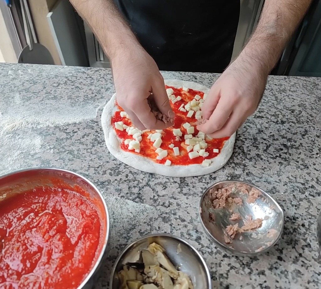 Ajout deffiloché de thon et de tranches dartichauts sur la pizza comme garniture finale.