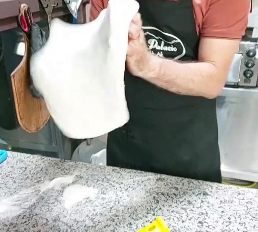 Une base de pâte à pizza en forme de disque façonnée par un mouvement de lancer en lair.