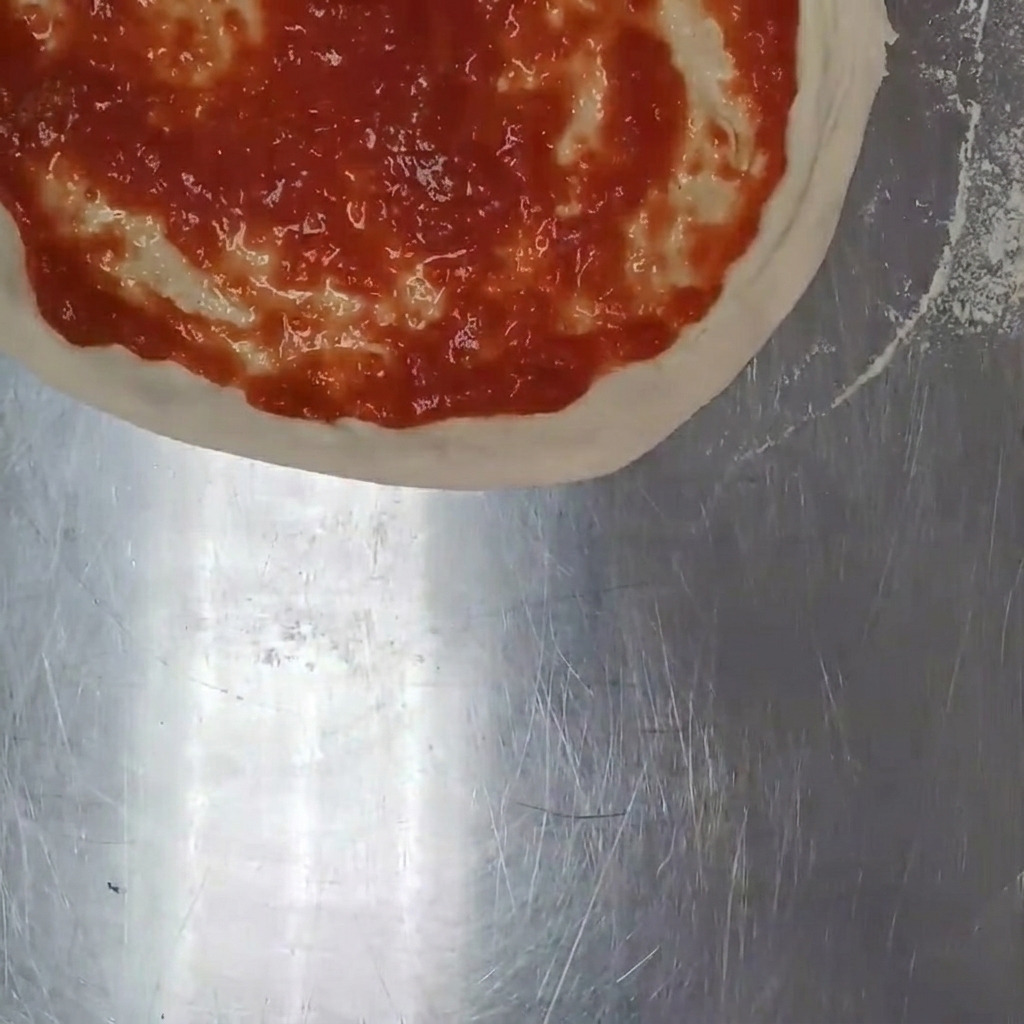 Des morceaux de mozzarella fraîche éparpillés à la main sur la sauce tomate de la pizza.