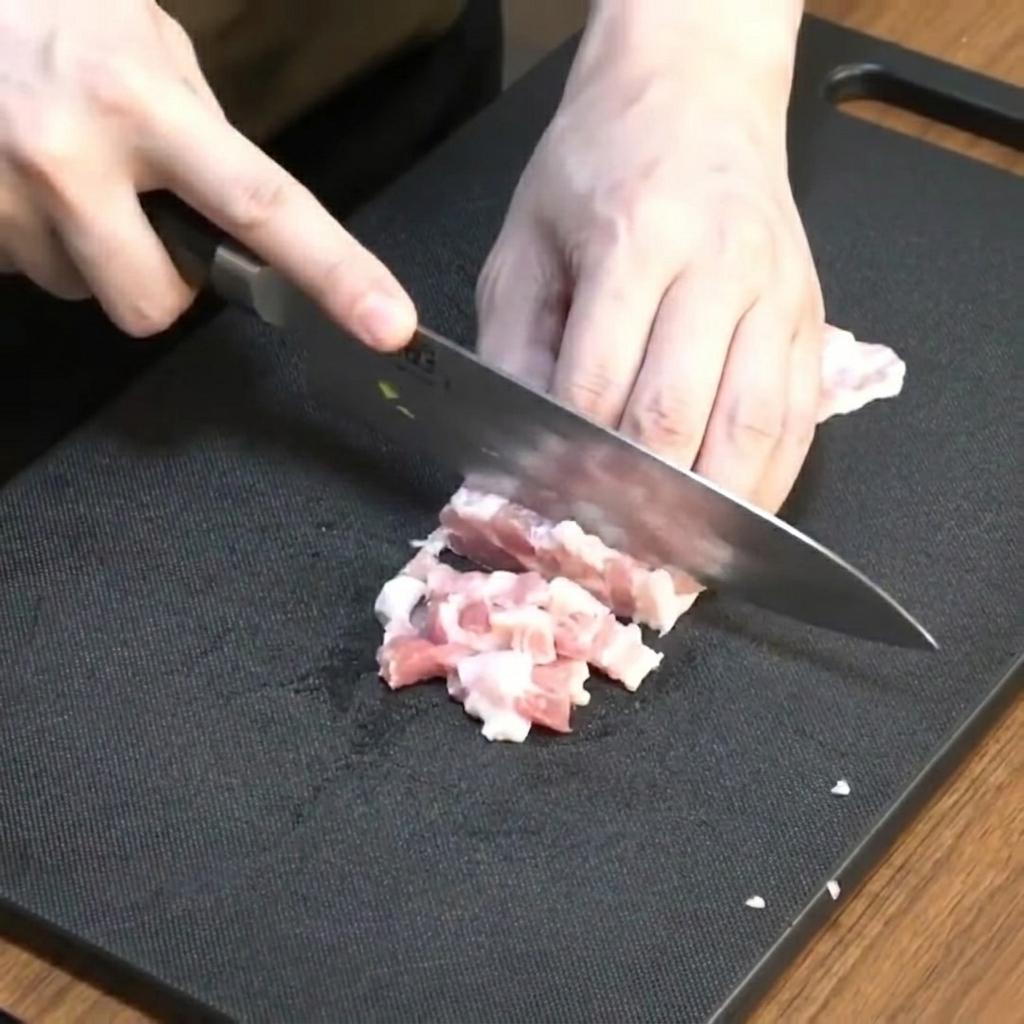 De la poitrine de porc crue soigneusement coupée en petits morceaux sur une planche.